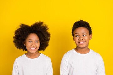Portrait of positive minded siblings look interested each other isolated on yellow color background