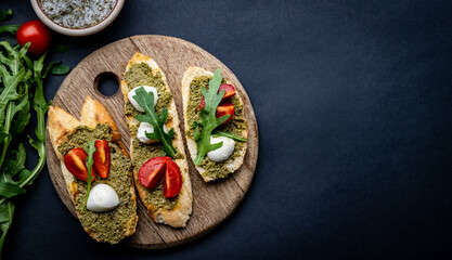 Fototapeta na wymiar Bruschettas with pesto, tomatoes, mozzarella cheese and basil on wooden board. Italian tosted bread with vegetables and traditional sauce