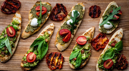 Fototapeta na wymiar Set of bruschettas with pesto, guacamole, grilled tomatoes, mozzarella cheese, basil and arugula on wooden board. Italian tosted bread with vegetables and traditional sauces