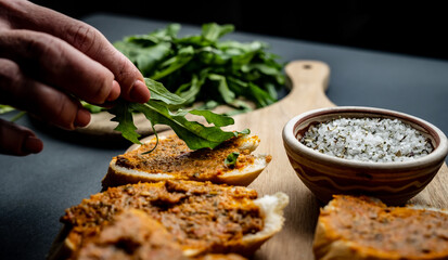 Person hand decorate bruschettas with pesto and arugula and served them on wooden board with salt...