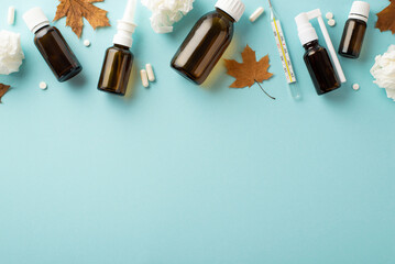 Seasonal diseases concept. Top view photo of medicines transparent brown spray and syrup bottles pills capsules maple leaves and crumpled napkins on isolated pastel blue background with copyspace