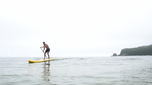 An athlete on a large yellow SUP with a paddle performs a turn trick in turquoise water. Active rest.