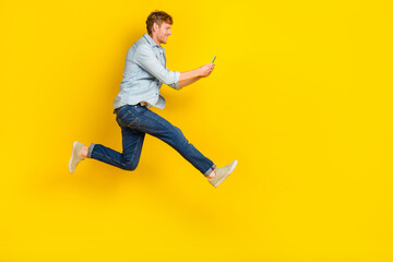 Fototapeta premium Full size photo of handsome guy red hair blue shirt jeans sneakers chatting listen notification online isolated on yellow color background