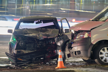 Damaged in heavy car accident vehicles after collision on city street crash site at night. Road...