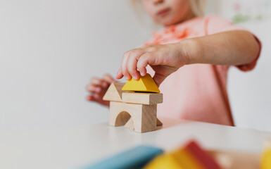 Little child girl playing wooden building blocks at home or kindergarten. Development and construction concept. Multi-colored educational bricks for early learning and education for young children.