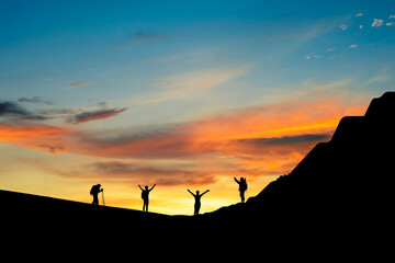 Silhouette of small group young traveler standing open arms on top of the mountain in the morning. They was delighted and happy to come and see the sunrise from the top of the mountain.