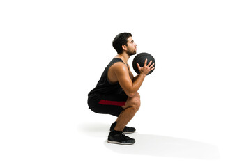 Side view of an active man training doing squats with a slam ball