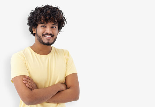 Portrait of happy Asian man guy with curly hair and white teeth in a yellow t-shirt standing on a white background looking at camera and smiles friendly, copy space