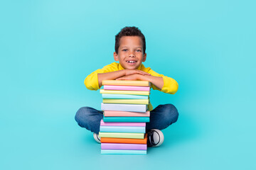 Full size photo of positive boy sit floor big pile stack book have good mood isolated on teal color...