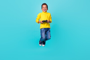 Full size photo of energetic excited little boy jump hands hold gamepad have fun isolated on turquoise color background © deagreez