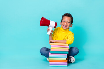 Full length photo of small cheerful boy sitting floor pile stack book hand hold loudspeaker...