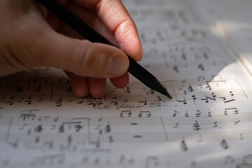 Close-up of the hands of a musician or composer writes a piece of music. Conservatory, music, composer, sheet music, lessons, artistic life concept. Sheet with music notes and pencil