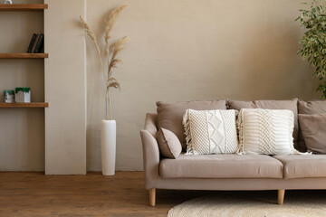 Sofa with macrame cushions on a woven round rug in a modern living room in beige tones. Cozy...