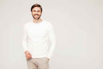 Fototapeta premium Portrait of handsome smiling hipster lumbersexual businessman model wearing casual white sweater and trousers. Fashion stylish man posing against grey background in studio