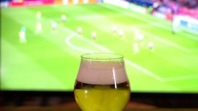 Pint of beer on the table in front of television show off football.