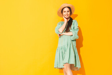 Young beautiful smiling female in trendy summer green dress. Sexy carefree woman posing near yellow wall in studio. Positive model having fun. Cheerful and happy. In hat. Isolated