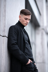 Portrait of a young attractive guy in dark clothes on the street