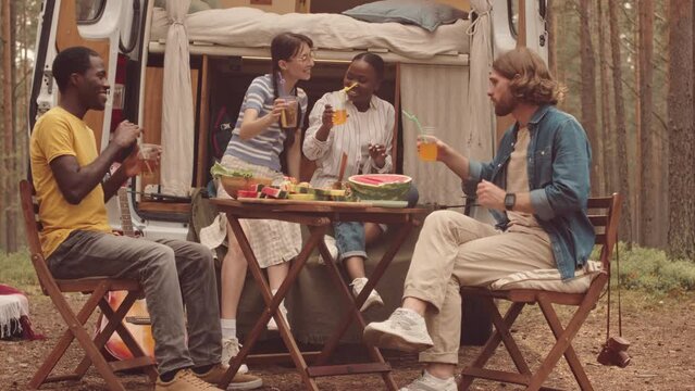 Four young multiethnic male and female friends toasting with plastic cups while having trailer party at campsite