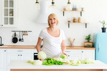 Beautiful blonde girl pregnant blonde in the kitchen in Scandinavian style at the table parses green cabbage