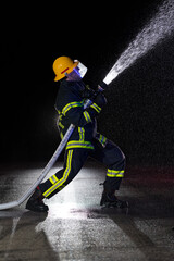 Firefighter in fire fighting operation. Portrait of a heroic fireman in a protective suit and red helmet in action during heavy rain.