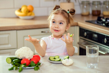 A happy girl 2-3 years old in the kitchen at home or in kindergarten eats delicious and healthy...