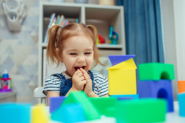 The little girl plays with colorful toy blocks and builds a tower. Educational and creative toys and games for young children.