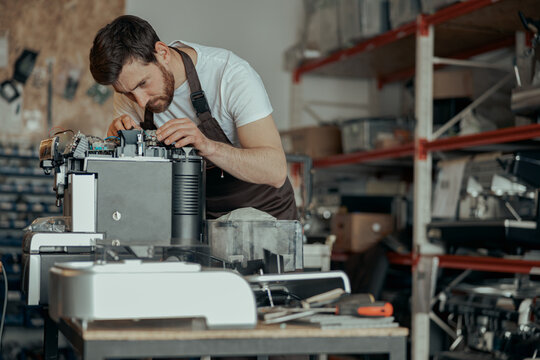 Man worker in uniform checking coffee machine in own workshop