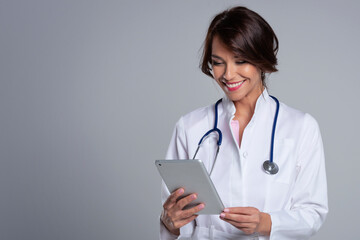Smiling female doctor with digital tablet standing at isolated grey background
