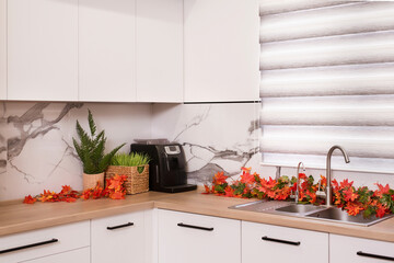 Autumn kitchen interior. Red and yellow leaves and flowers in the vase and pumpkin on light background