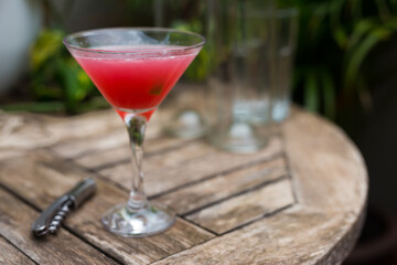 red cocktail with ice in glass with stem on wooden surface