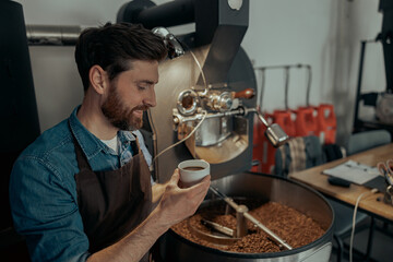Close up of male barista holding cup of coffee on background of roasting coffee machine