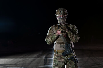 Army soldier in Combat Uniforms with an assault rifle, plate carrier and combat helmet going on a dangerous mission on a rainy night. 