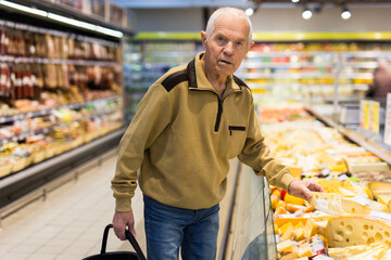 elderly man choosing cheese in supermarket