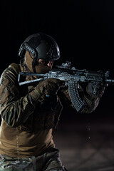 Army soldier in Combat Uniforms with an assault rifle, plate carrier and combat helmet going on a dangerous mission on a rainy night. 