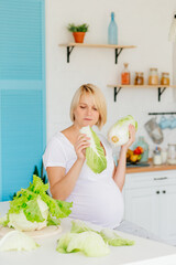 Beautiful blonde girl pregnant blonde in the kitchen in Scandinavian style at the table parses green cabbage 