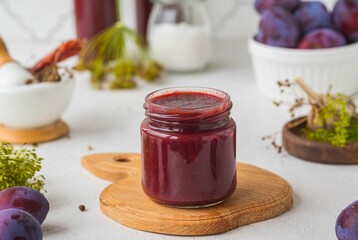 Tkemali, spicy plum sauce in a glass jar on a light concrete background. Fruit sauces,...