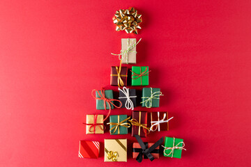 Image of christmas gifts forming christmas tree and copy space on red background