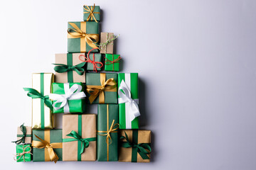 Image of christmas gifts forming christmas tree and copy space on grey background