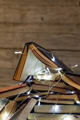 Image of christmas decoration with fairy lights and stack of books on wooden background