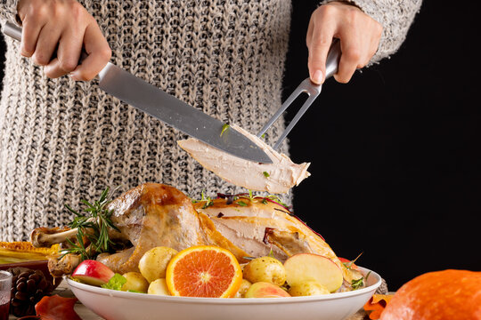 Close up of caucasian woman carving thanksgiving roast turkey with vegetables