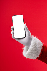 Image of hand of santa claus holding smartphone with blank screen and copy space on red background © vectorfusionart