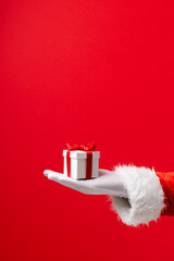 Obraz na płótnie Canvas Image of hand of santa claus holding christmas gift with copy space on red background