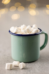 Image of green mug with christmas marshmallows with copy space and fairy lights in background