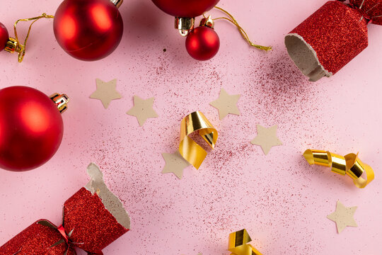 Image of christmas red baubles and christmas cracker decoration on pink background