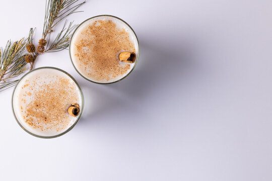 Image of two glasses of milk with cinnamon sticks christmas decorations copy space on white