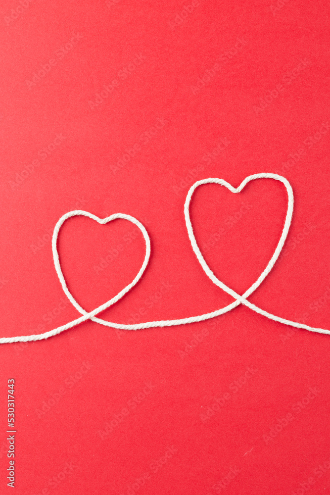 Wall mural Vertical image of hearts made of white string on red surface