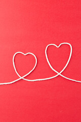 Vertical image of hearts made of white string on red surface