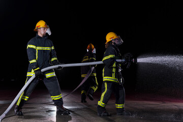 Fototapeta premium Firefighters using a water hose to eliminate a fire hazard. Team of female and male firemen in dangerous rescue mission. 