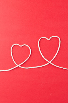 Vertical image of hearts made of white string on red surface