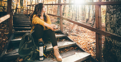 Woman tourist is enjoying fall nature and holds warm thermos in hands.